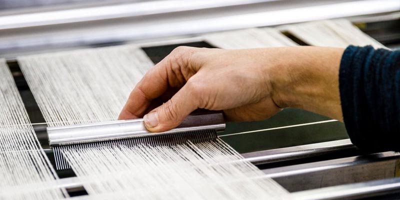 A sewing machine stitching fabric, with a knitted sweater in the background