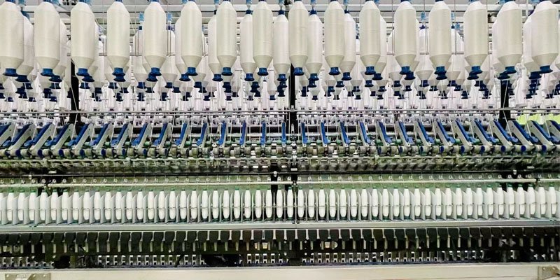 A close-up of a compact spinning machine in operation, showing yarn being formed.